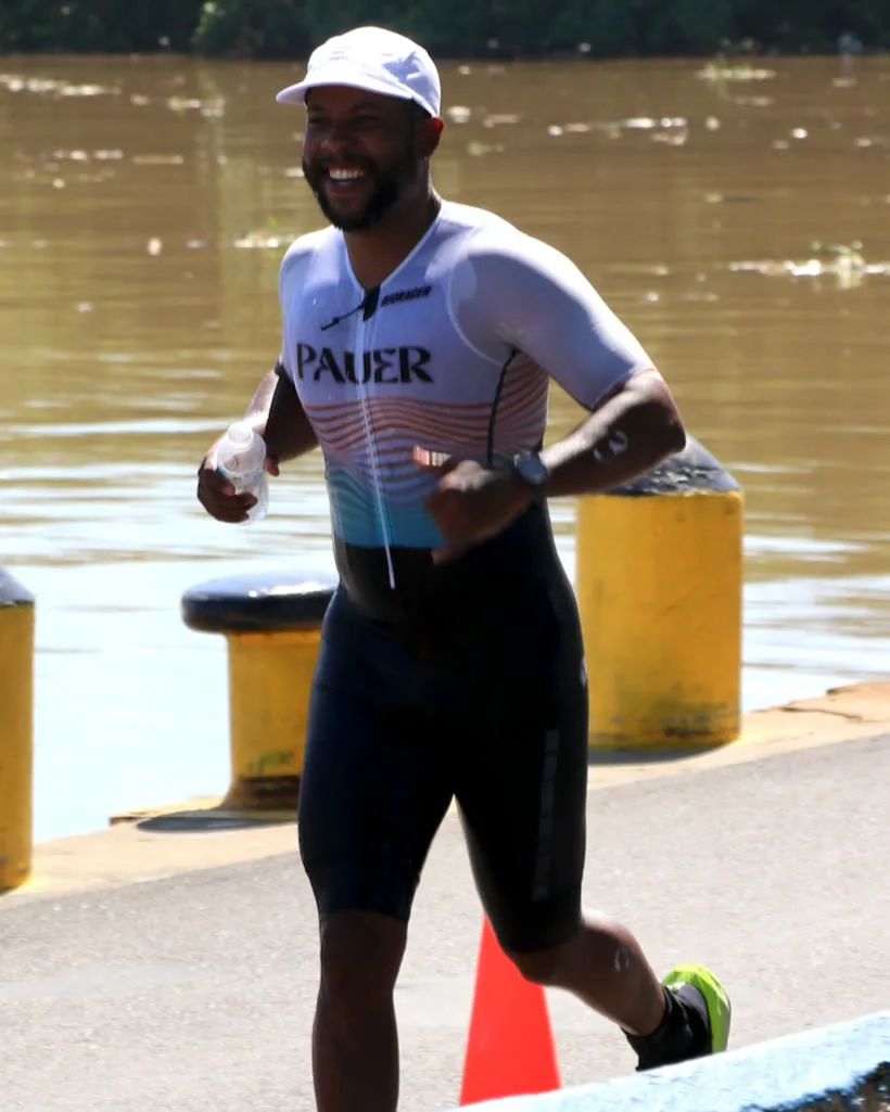 Atleta con el uniforme PAUER corriendo sonriente junto al río en una competencia